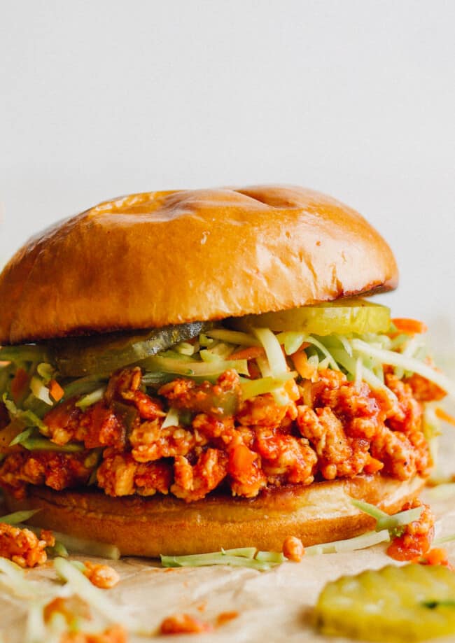 up close image of chicken sloppy joes topped with slaw and pickles