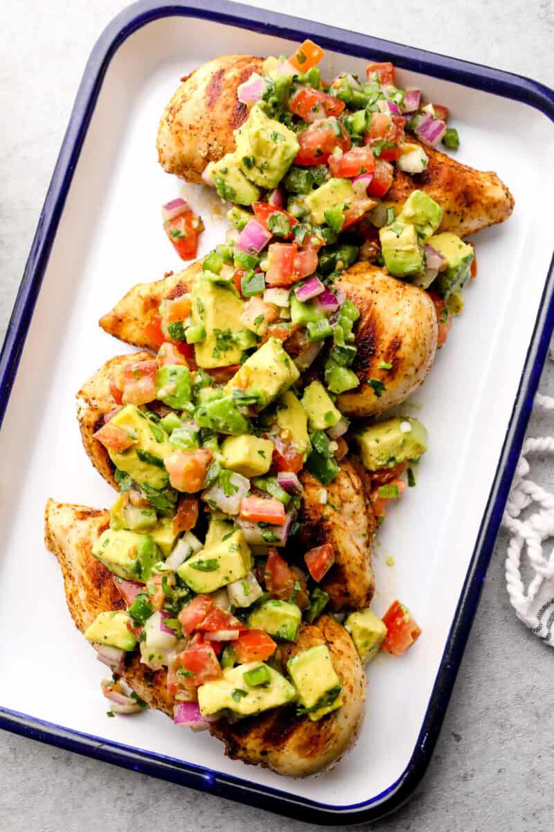 grilled chicken breasts topped with avocado salsa on platter