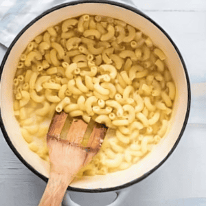 stirring elbow macaroni into a pot with a wooden spatula.