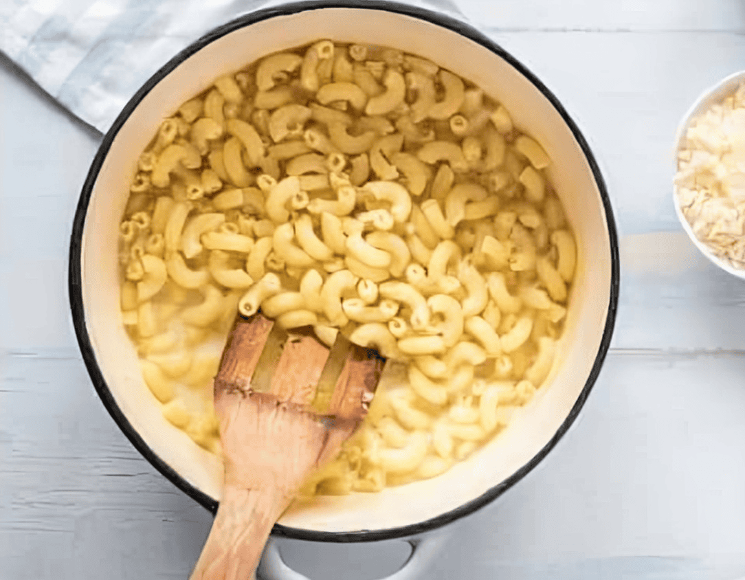 stirring elbow macaroni into a pot with a wooden spatula.