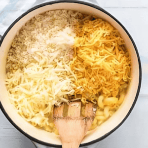 stirring cheeses into cooked macaroni in a pot with a wooden spatula.