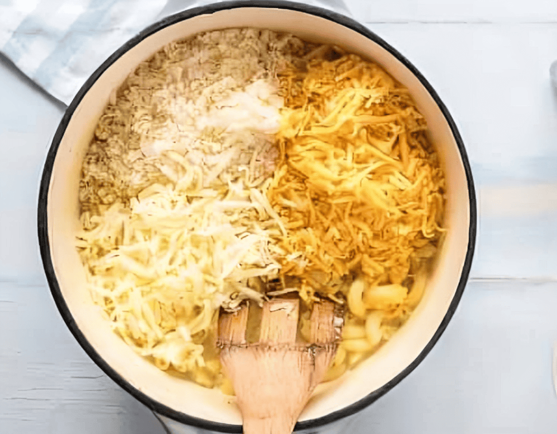 stirring cheeses into cooked macaroni in a pot with a wooden spatula.