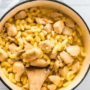 stirring chicken mac and cheese in a pot with a wooden spatula.