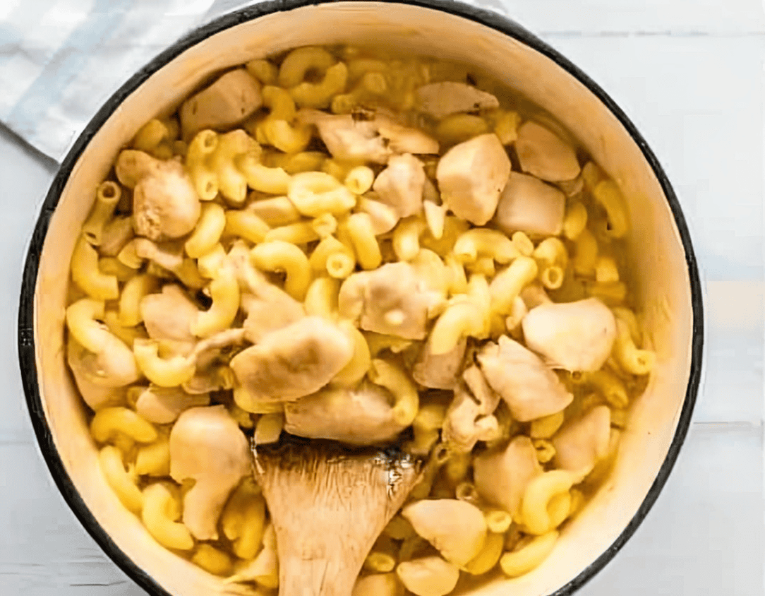 stirring chicken mac and cheese in a pot with a wooden spatula.