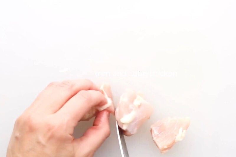 cubing chicken on a cutting board.