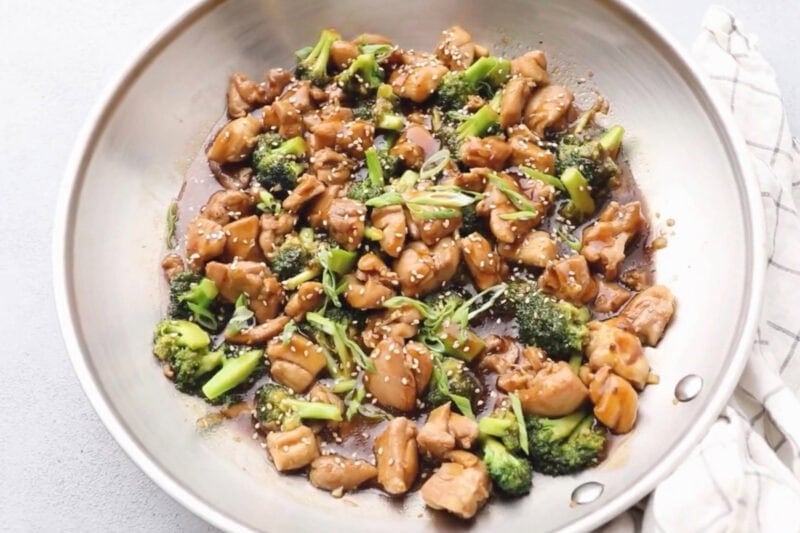 teriyaki chicken thighs with broccoli and green onions in a pan.