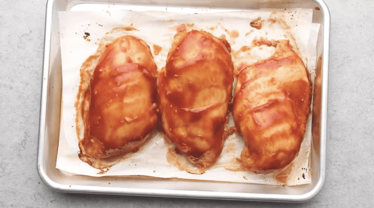 Raw chicken breasts are coated with bbq sauce. 