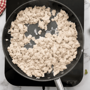 A person is frying chicken in a frying pan, preparing delicious chicken sloppy joes.
