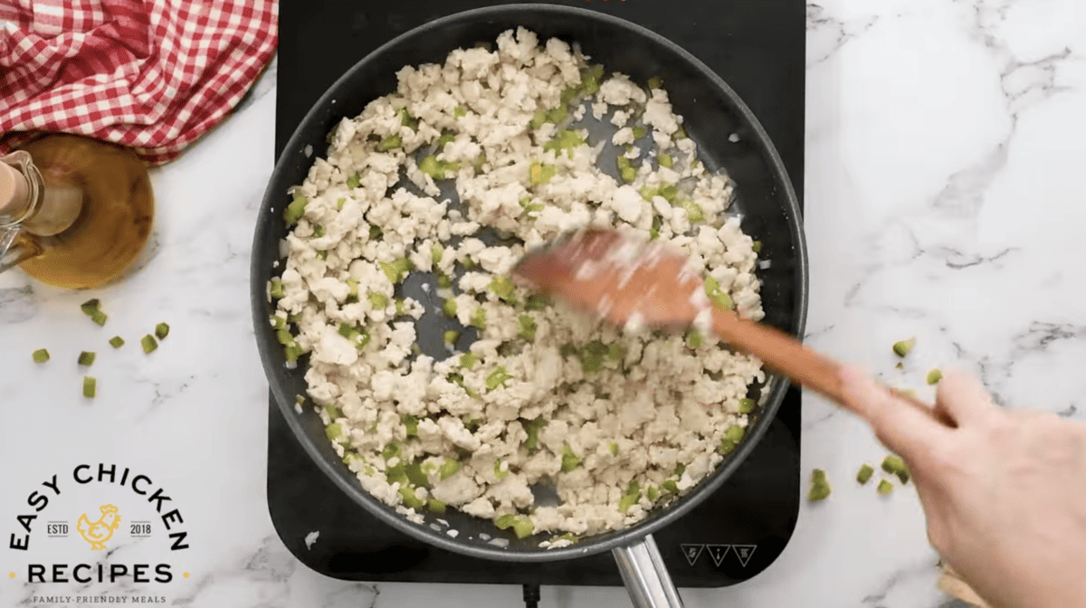 Chicken and veggies are cooking in a skillet. 