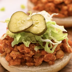 Shredded cabbage and pickles are placed on top of a chicken sloppy joe.