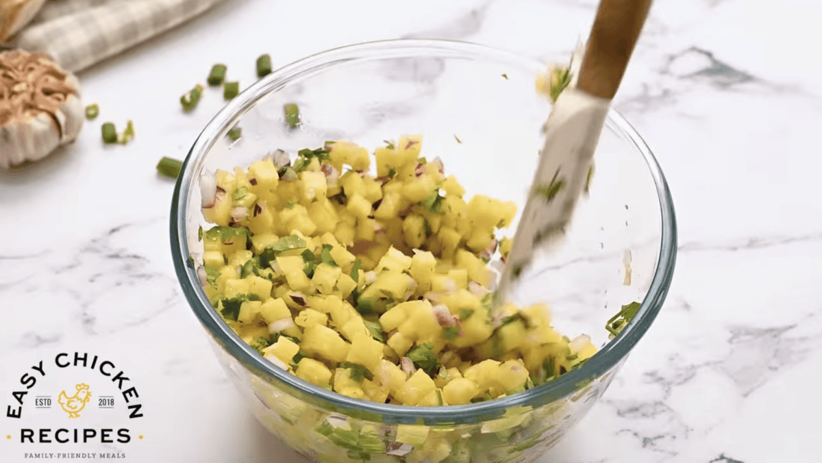 Pineapple salsa is being mixed in a glass bowl. 
