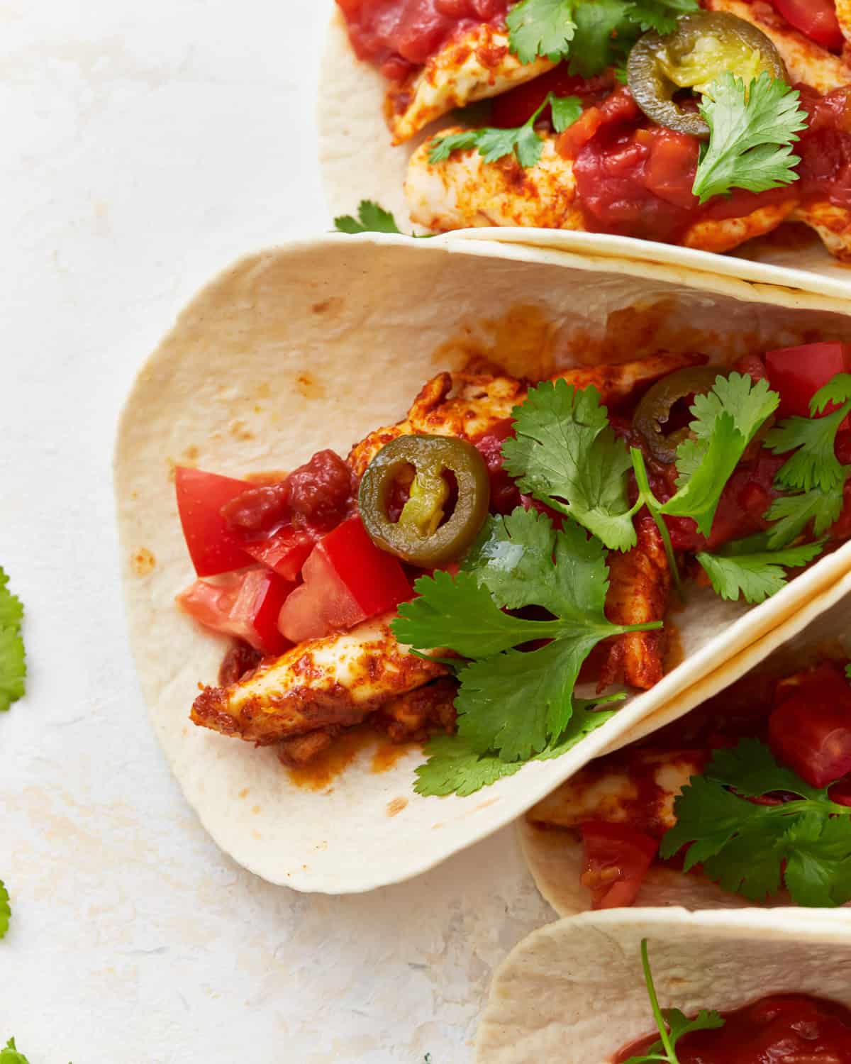 close up of a chicken taco topped with cilantro, tomatoes, and jalapenos.