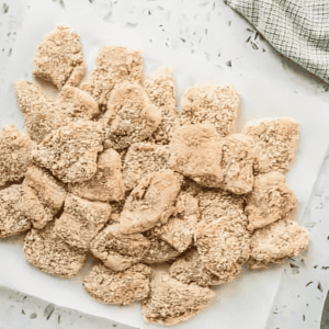 breaded raw chicken nuggets on a white plate.