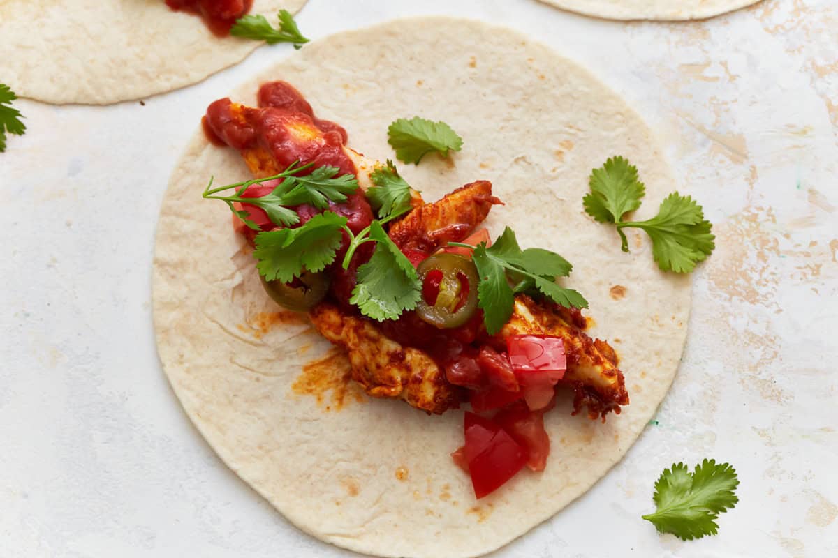 chicken strips topped with tomatoes, jalapenos, and cilantro on a tortilla.