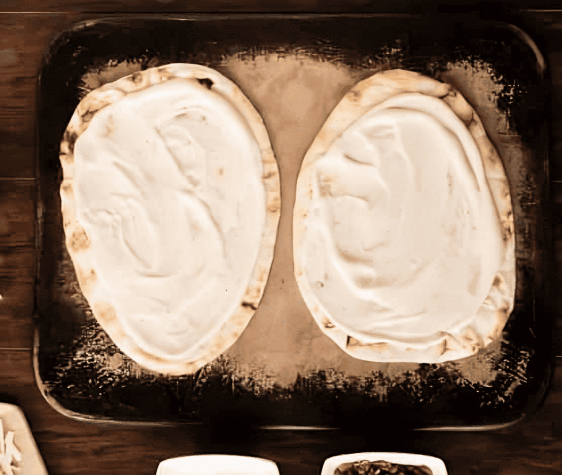 2 naan flatbreads spread with Alfredo sauce.