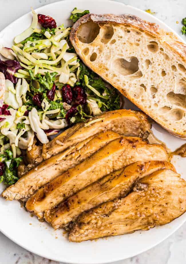 sliced bourbon chicken breast with bread and salad on plate