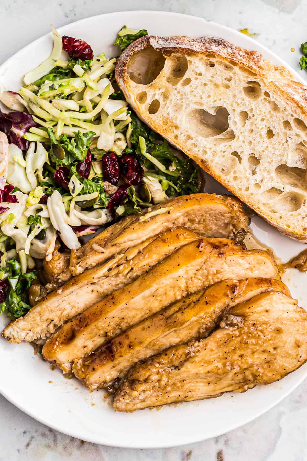 sliced bourbon chicken breast with bread and salad on plate