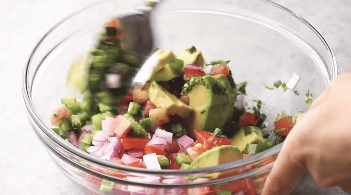 Avocado salsa is being prepared in a glass bowl. 
