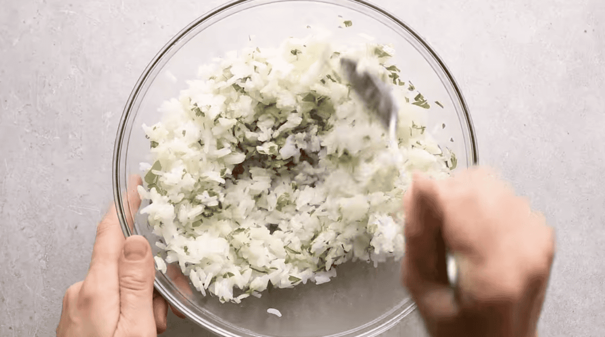 White rice is being mixed with cilantro and lime juice. 