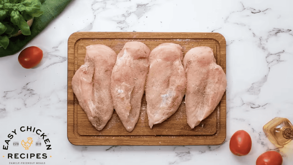 Chicken breasts are seasoned on a cutting board.