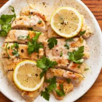 overhead view of 2 sliced creamy lemon chicken breasts with lemon slices on a white plate.