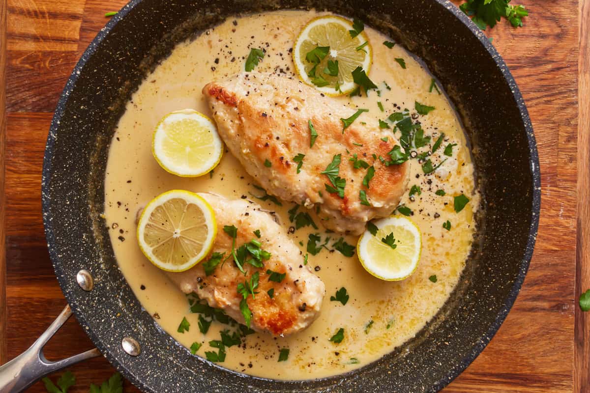 creamy lemon chicken in a skillet with lemon slices and parsley.