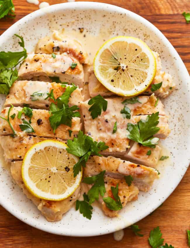 overhead view of 2 sliced creamy lemon chicken breasts with lemon slices on a white plate.