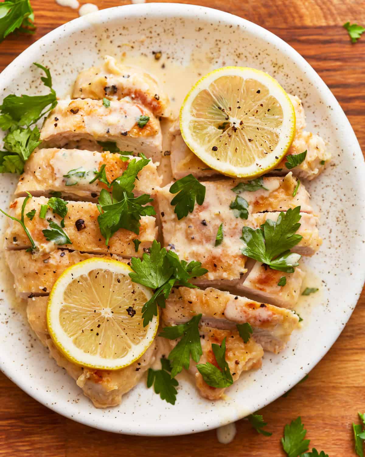 overhead view of 2 sliced creamy lemon chicken breasts with lemon slices on a white plate.