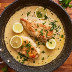 creamy lemon chicken in a skillet with lemon slices and parsley.