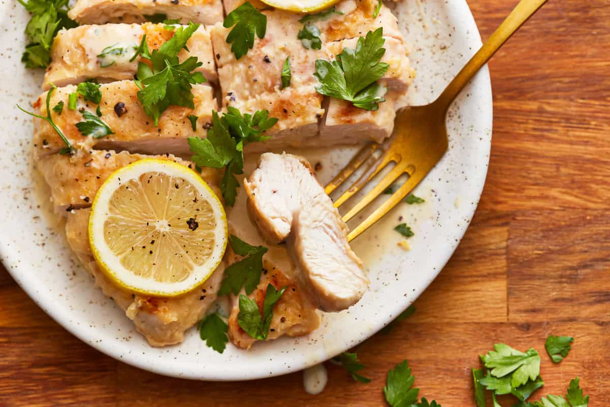 sliced creamy lemon chicken on a white plate with a fork.