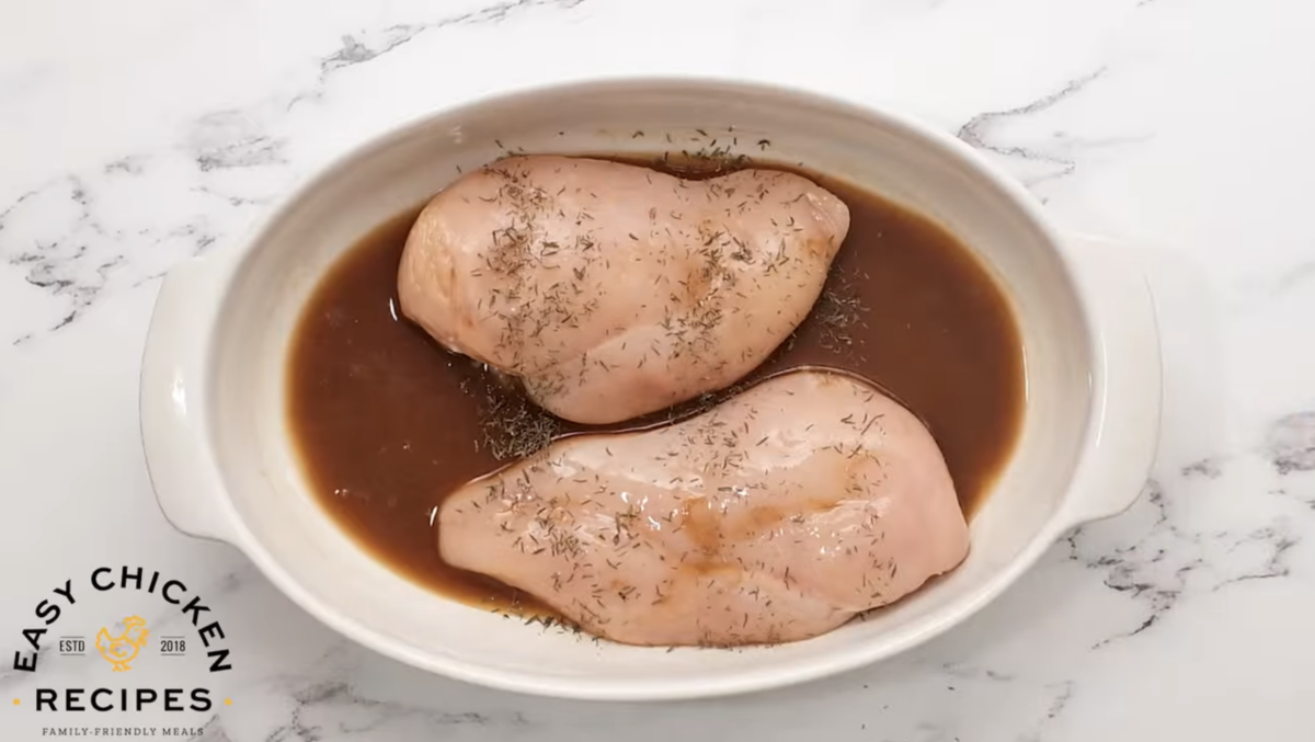 Two chicken breasts are in a baking dish with lemon sauce. 