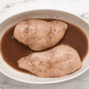 Two chicken breasts are in a baking dish with lemon sauce.