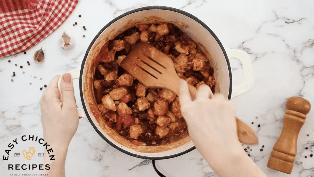 Chicken chili is being cooked in a pot with a wooden spatula. 