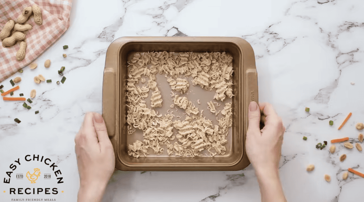 Uncooked ramen noodles are crushed and spread across a small baking pan. 