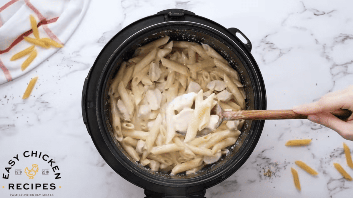 A wooden spoon is lifting a small portion of chicken and pasta from the pressure cooker. 