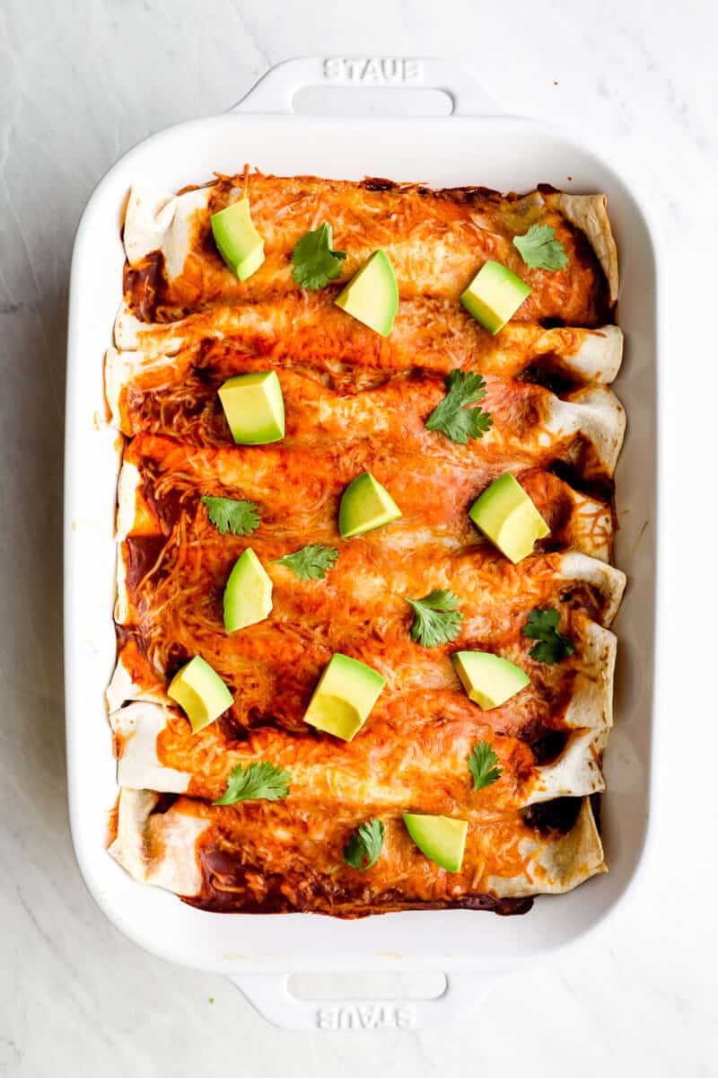 Chicken enchiladas with red sauce and avocado.