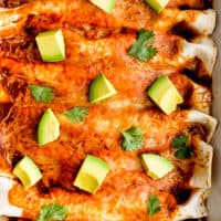 up close image of red chicken enchiladas topped with avocado