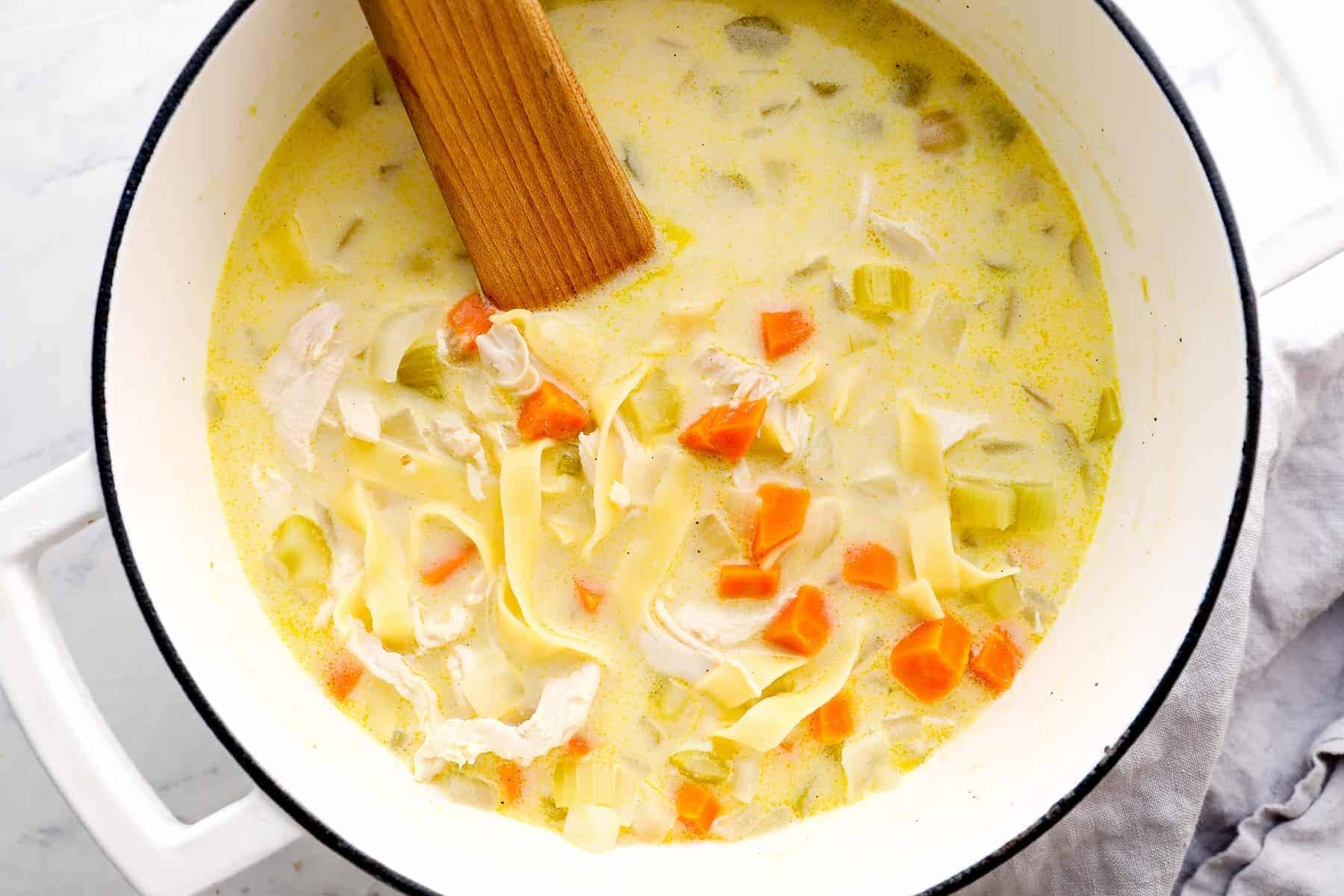 pot of creamy chicken noodle soup with wooden spoon