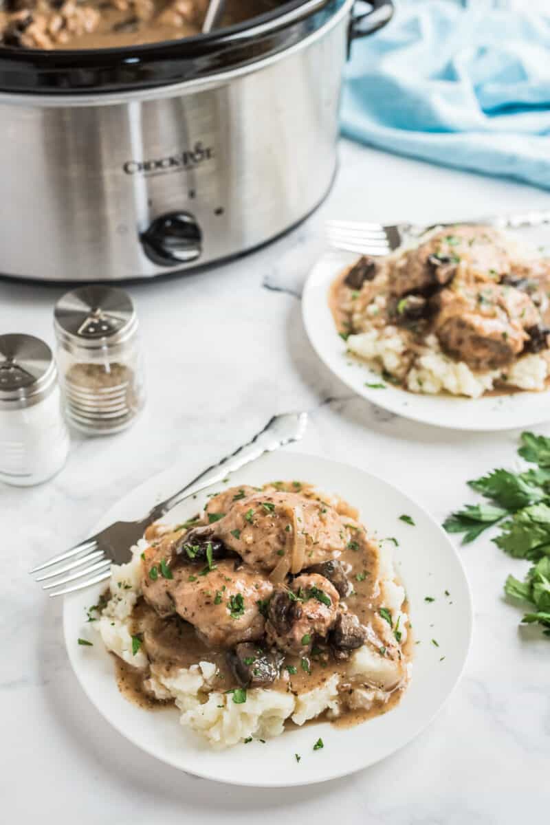 Two plates of chicken marsala next to crockpot.