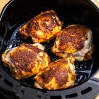 cooked chicken thighs in an air fryer basket.