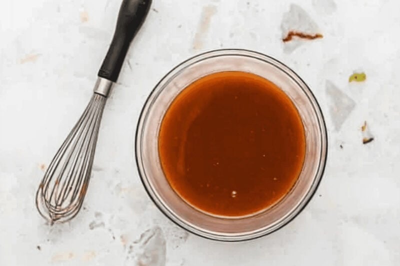 Buffalo sauce in a glass bowl with a whisk.