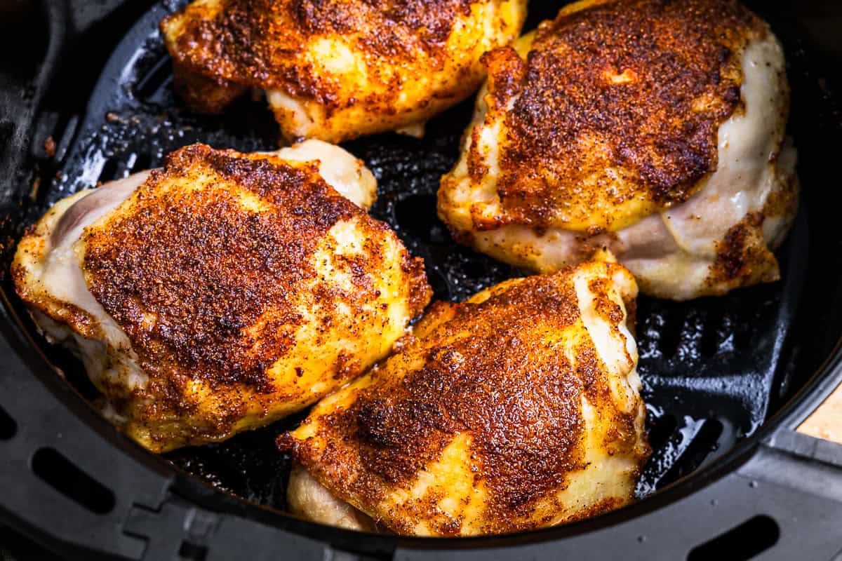 close up of cooked chicken thighs in an air fryer basket.