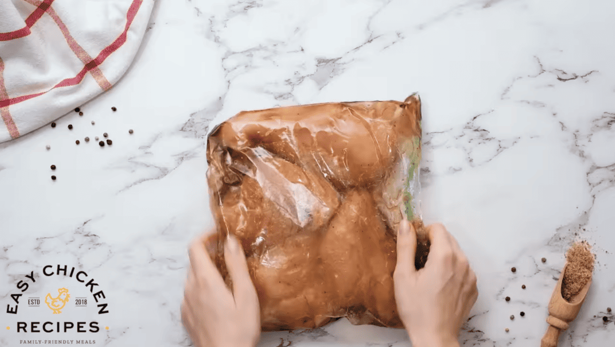 Chicken breasts are being marinated in a bag. 