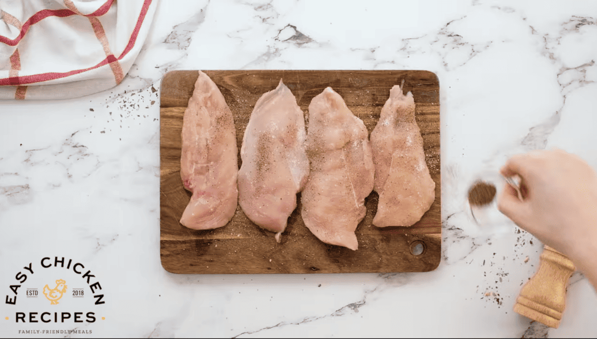 Chicken breasts are being sprinkled with salt and pepper. 