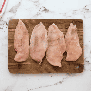 Chicken breasts are being sprinkled with salt and pepper.