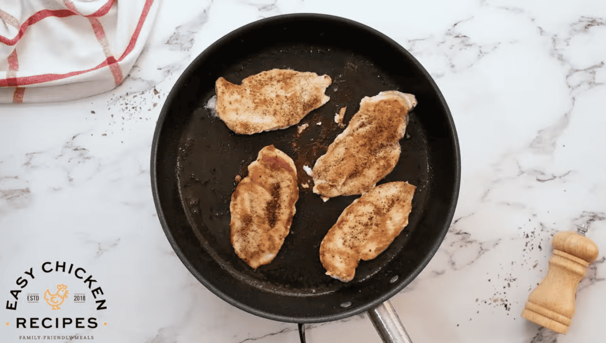 Chicken breasts are sizzling in a skillet. 