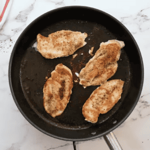 Chicken breasts are sizzling in a skillet.