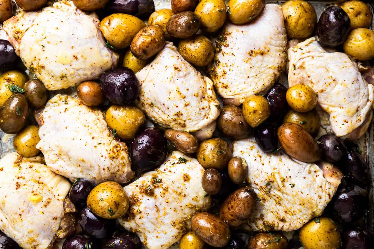 overhead view of unbaked honey mustard chicken thighs and baby potatoes on a sheet pan.