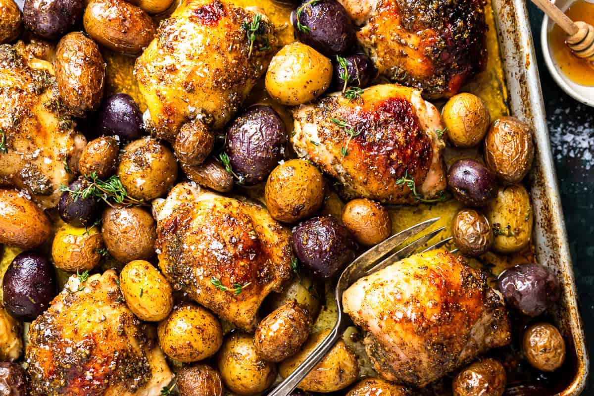 baked honey mustard chicken thighs and potatoes on a baking sheet.