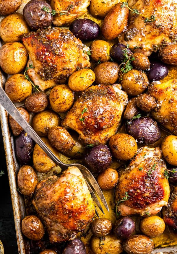 baked honey mustard chicken thighs and potatoes on a baking sheet with a fork.